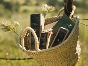 A woven basket hanging from a metal fence outside with Mēnos products inside. 