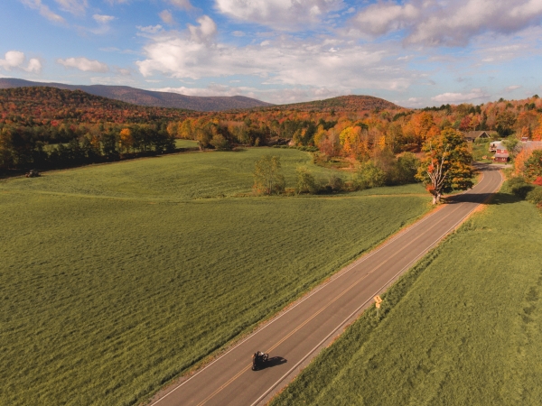 Person motorcycling on a long road with fields and mountains in the Catskills