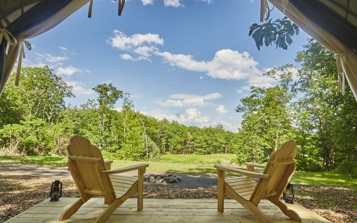 wooden chairs overlooking a fire pit from a glamping cabin deck
